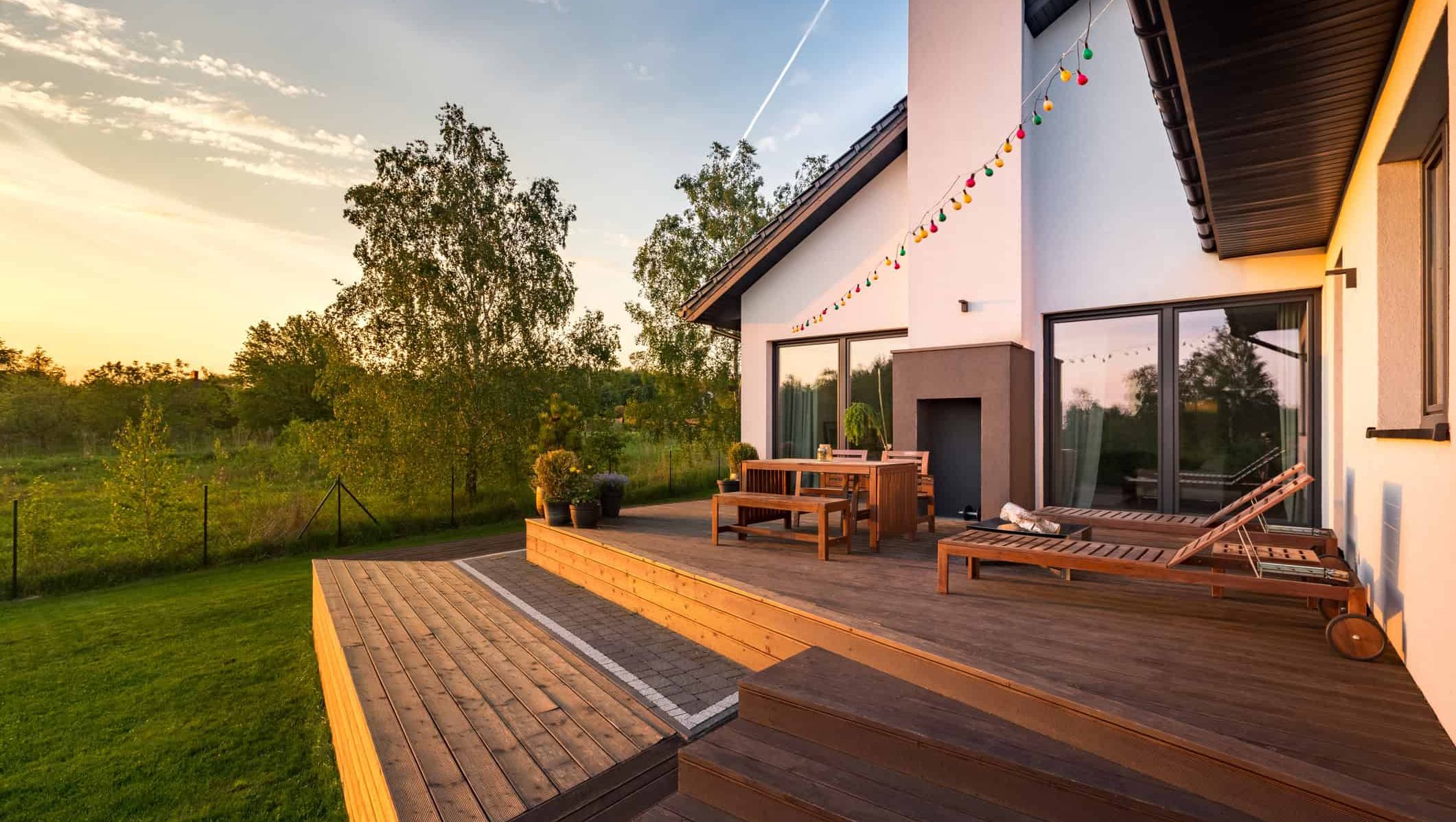Moderne terrasse med utemøbler, solsenger og lyslenke ved bolig i varmt kveldslys.